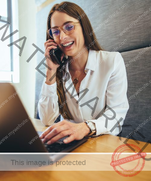 Happy entrepreneur smiling during a phone call. Cheerful young businesswoman communicating with her business partners. Female business professional working in a modern workspace.